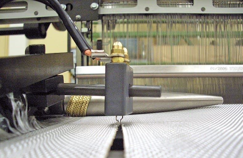 Close-up of an industrial weaving machine needle interacting with white fabric on a loom.