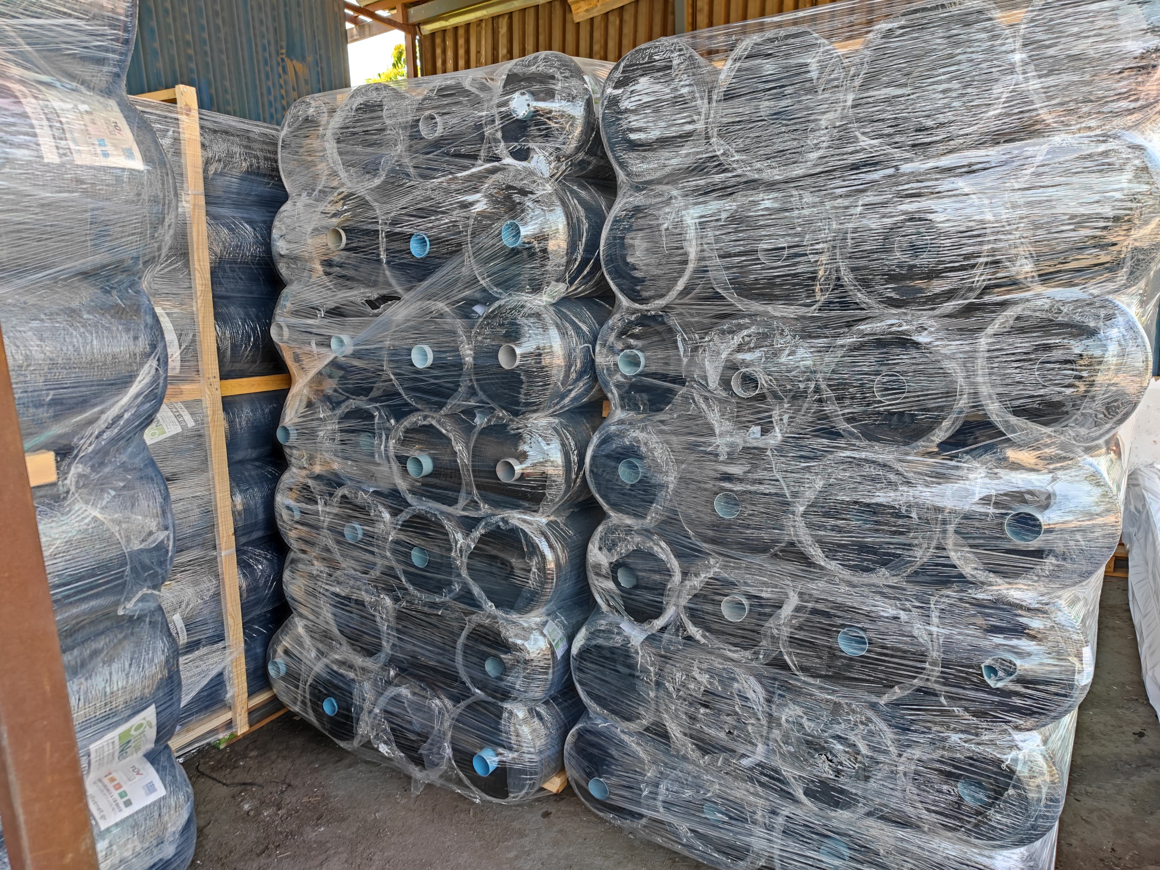 Stacks of black industrial netting rolls wrapped in clear plastic film on wooden pallets.